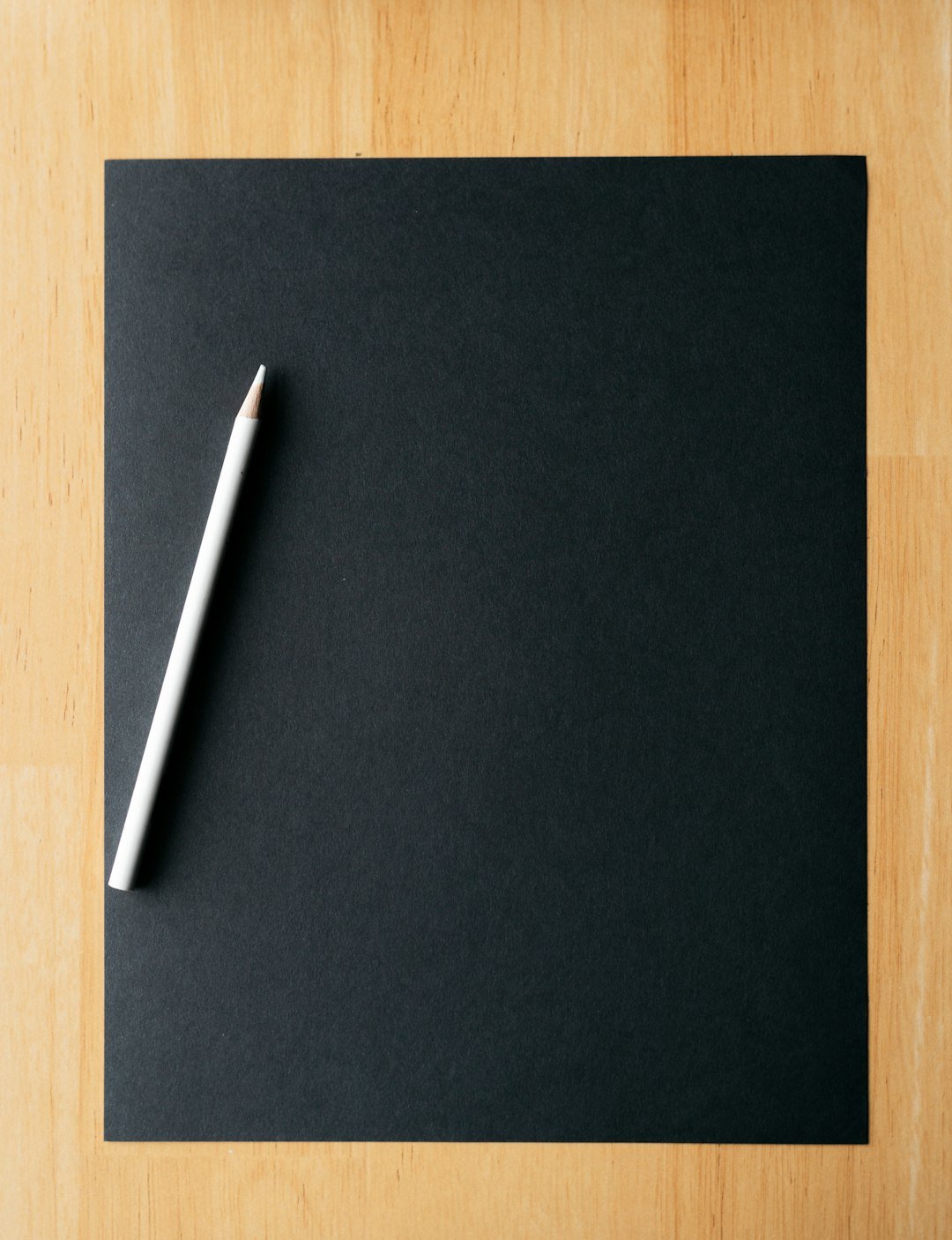 White pencil rests on a blank, black paper.